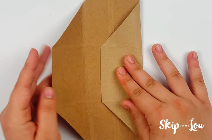 Two hands folding the right side of the cardboard inwards using the folded guideline.