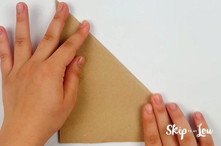 Two hands folding the brown sturdy paper in half at a 45-degree angle. 