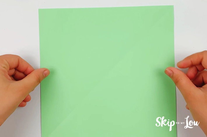 Two hands holding a green square piece of paper. 