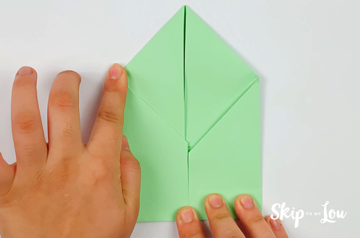 Two hands folding the left and right bottom flaps inwards towards the center line.
