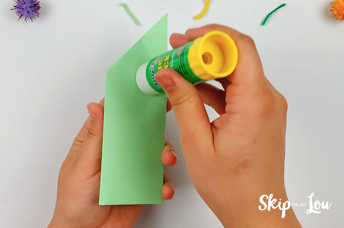 Two hands applying some glue to the side of a paper pen holder. 