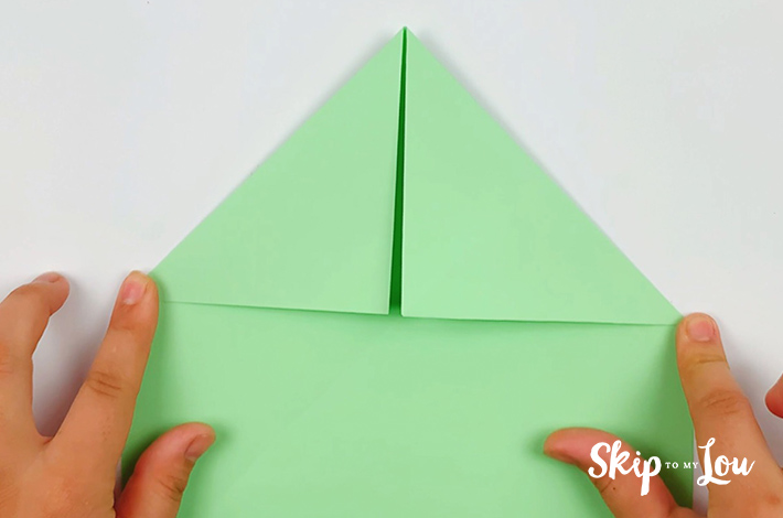 Two hands folding the top left and right and side of the paper to form two triangles.
