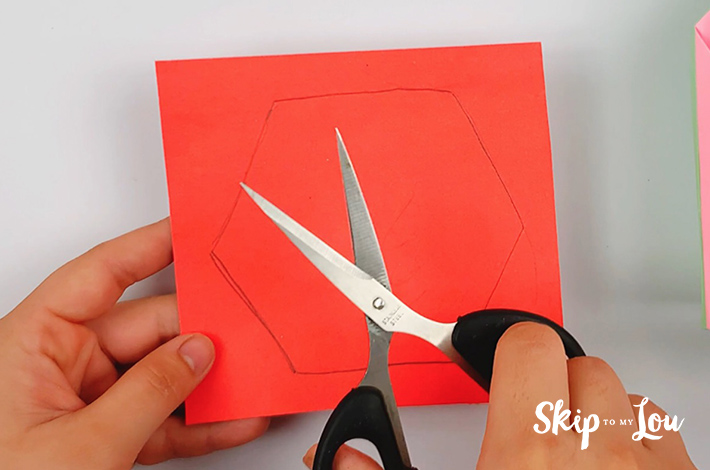 Two hands holding a square piece of paper with a hexagonal shape traced out from its underside.