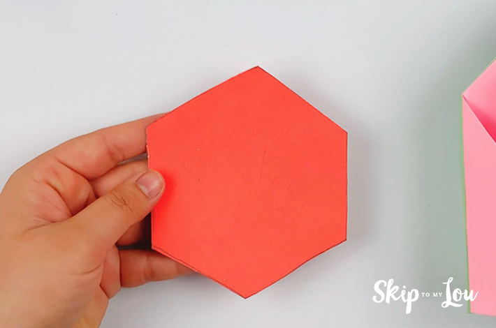 Two hands holding the hexagonal shape that has been cut out with a pair of scissors. 