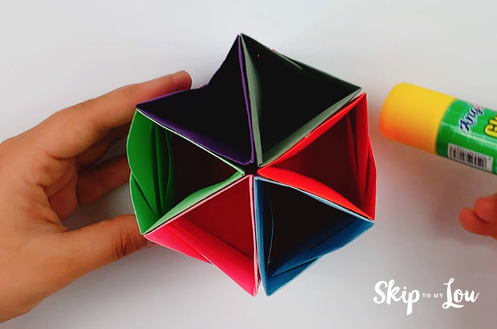 Two hands glueing the hexagonal shape to the bottom of the origami pen holder.