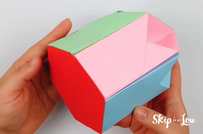 Two hands holding the origami pen holder with the glued underside visible.