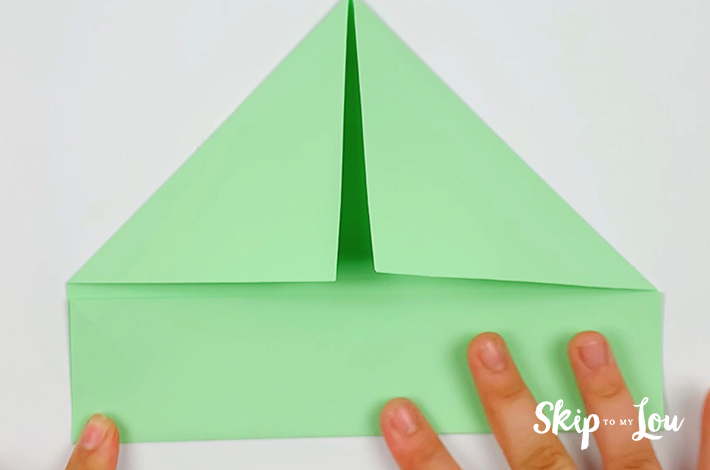 Two hands folding the bottom section of the paper upwards to a point just below the two folded triangles. 