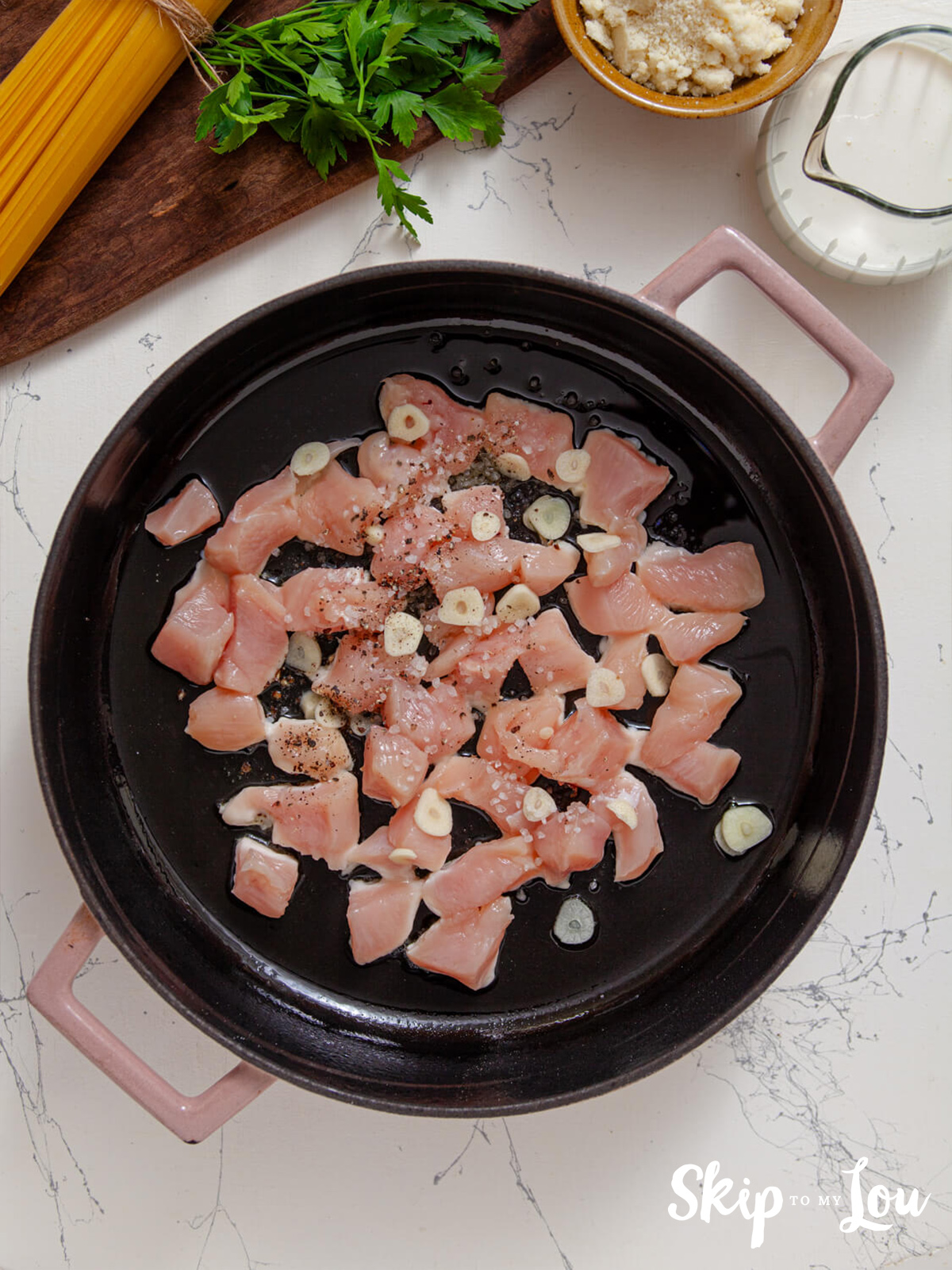 Chicken pieces in a skillet with olive oil, garlic, salt and pepper.