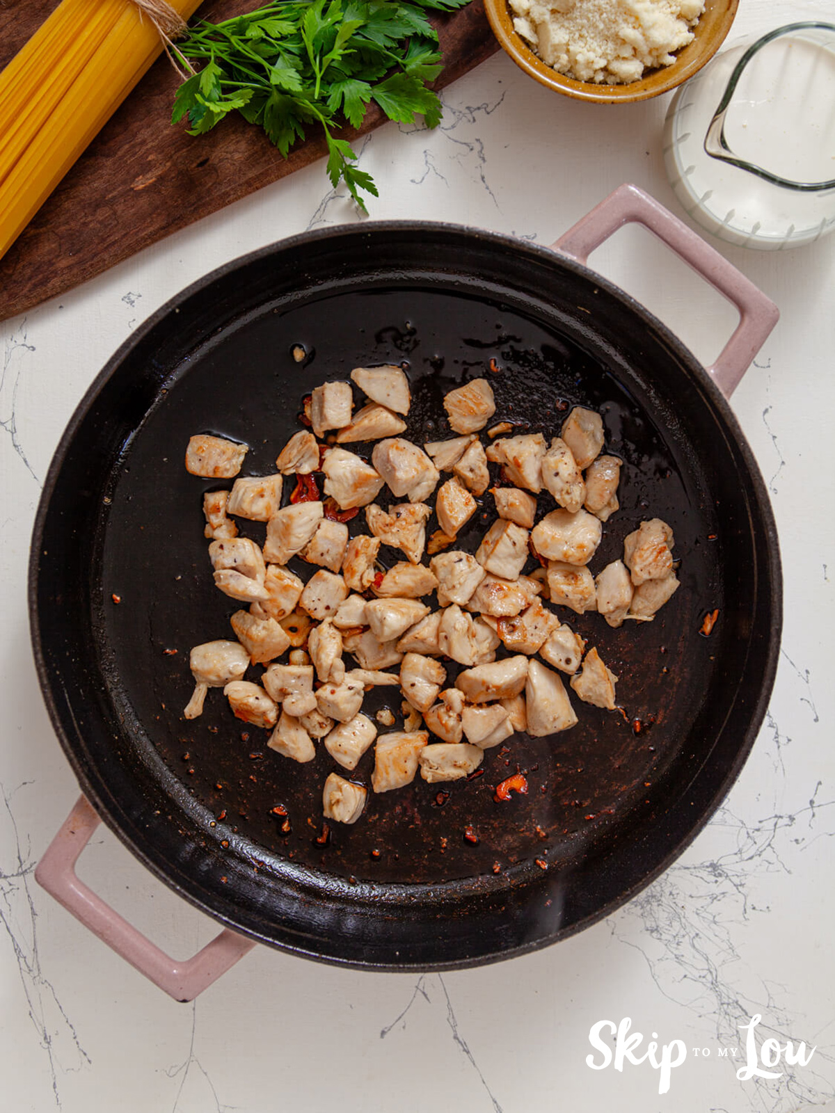Cooked Chicken pieces in a skillet with olive oil, garlic, salt and pepper.