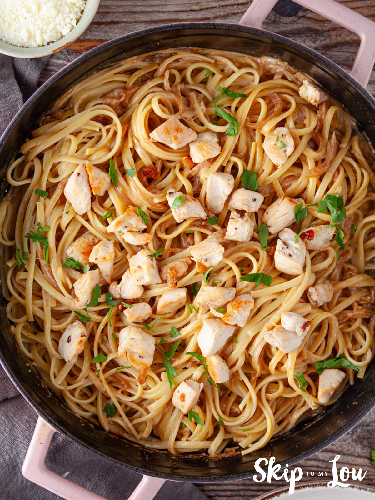 A skillet with caramelized onion sauce, linguine and topped with cooked chicken, parmesan, and parsely.