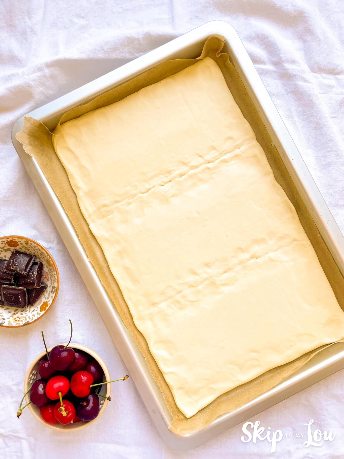 A baking tin lined with parchment paper and rolled out puff pastry placed inside. 