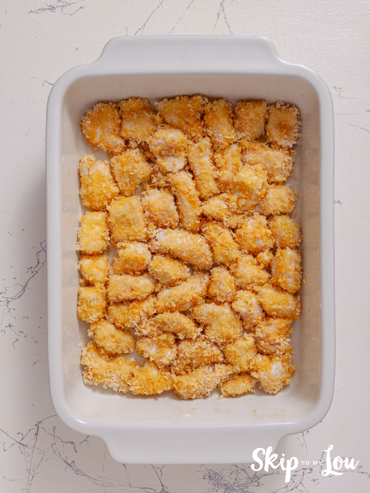 Coated chicken ina casserole dish ready to be baked. 