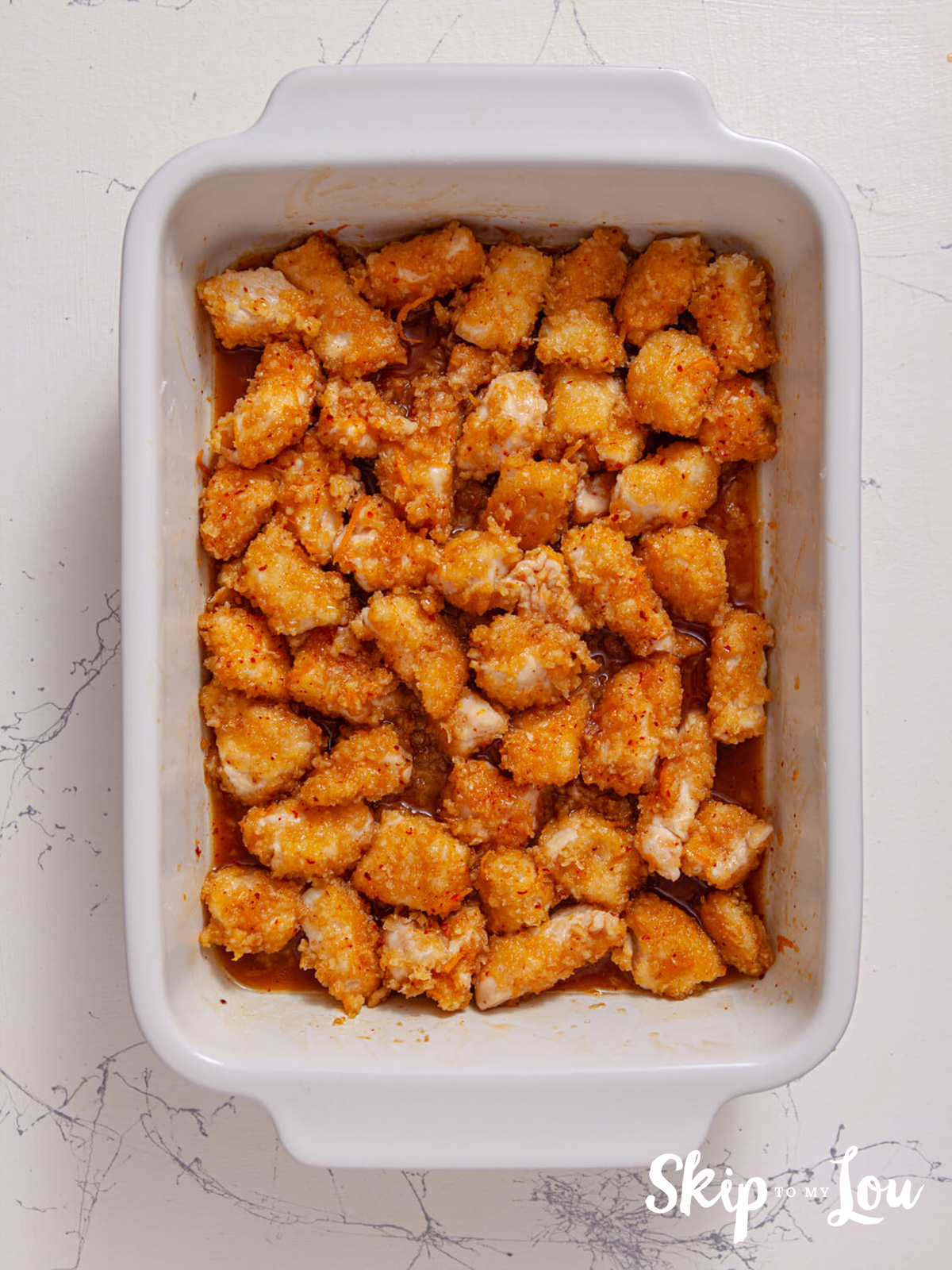 Chicken covered with the orange sauce and sitting in a casserole dish. 