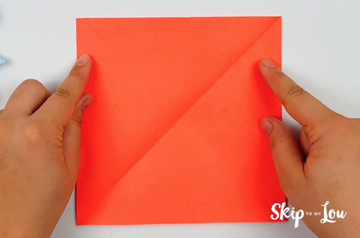 Two hands holding a square piece of red paper.