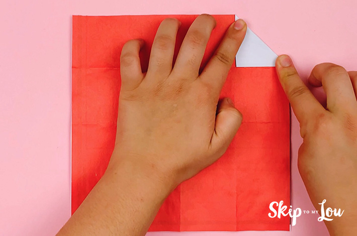 Two hands folding a triangle in the right hand top corner. 