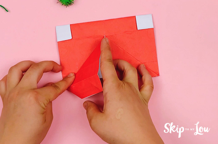 Two hands unfolding the bottom triangle and bringing as section of the paper downwards. 