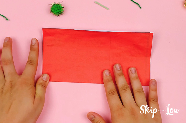 Two hands folding the square piece of paper in half. 