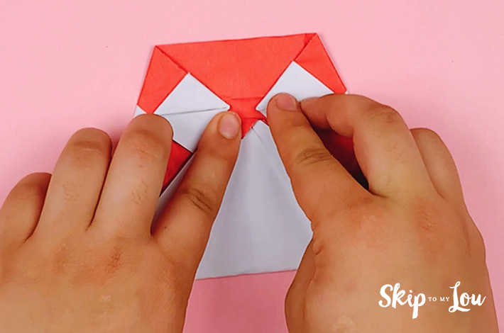 Two hands folding the small top triangle over to form the beak. 