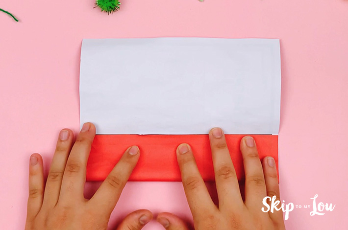Two hands folding the bottom of the paper up to the center crease line. 
