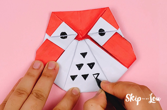 Two hands using a black marker to decorate the owl by adding eyes and feathers. 