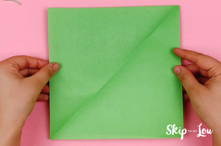 Two hands holding a green square piece of paper.