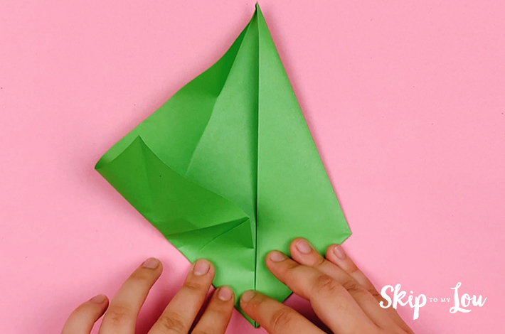 Two hands folding the bottom left side of the paper upwards.