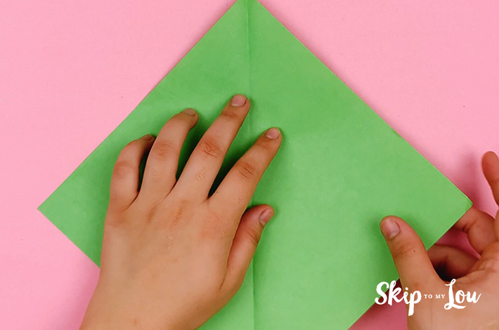 Two hands unfolding the first fold and turning the paper 45 degrees so it forms a kite shape.