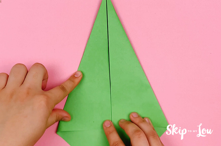 Two hands folding the left flap of the paper towards the crease line from the first fold.