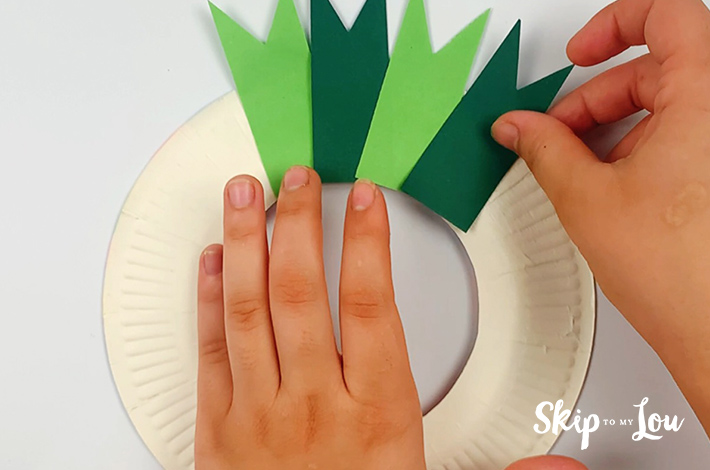 Two hands gluing more petals onto the paper plate.