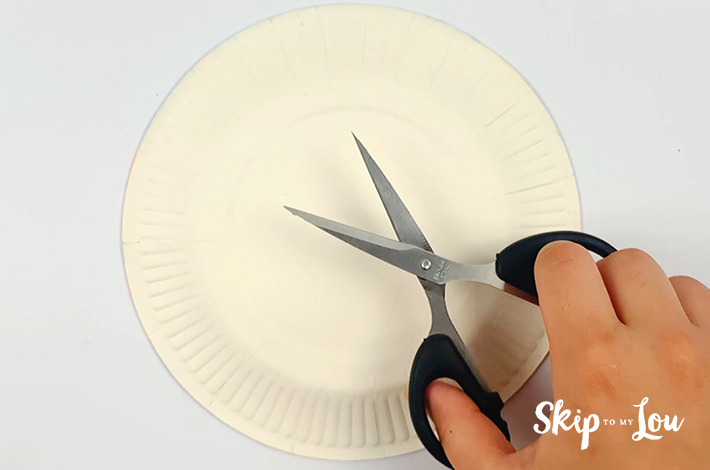 A hand holding a scissors and a paper plate below it.