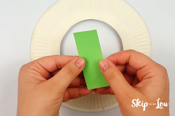 Two hands holding a piece of rectangular paper to form the wreath petals.