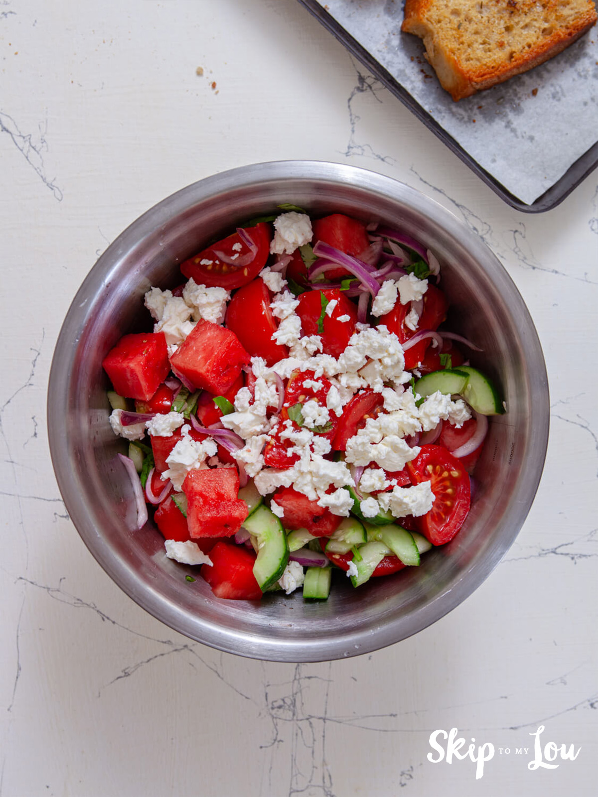 Watermelon, feta, basil, red onion and cucumber combined in a bowl. 