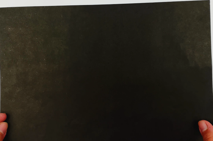Two hands holding a large piece of black square paper.