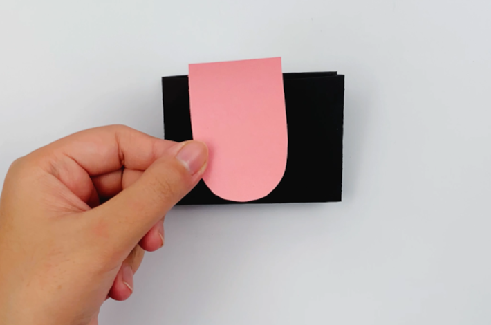 Two hands holding the cat's tongue cut from a piece of pink paper.