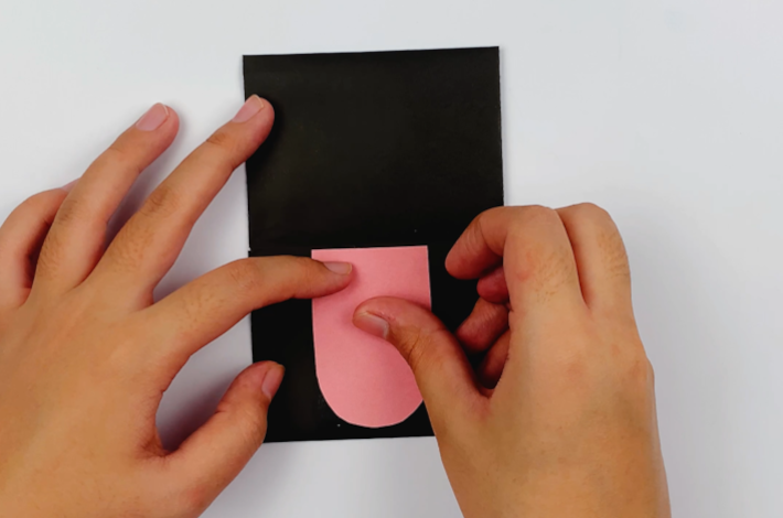 Two hands glueing the cat's tongue to the black paper.