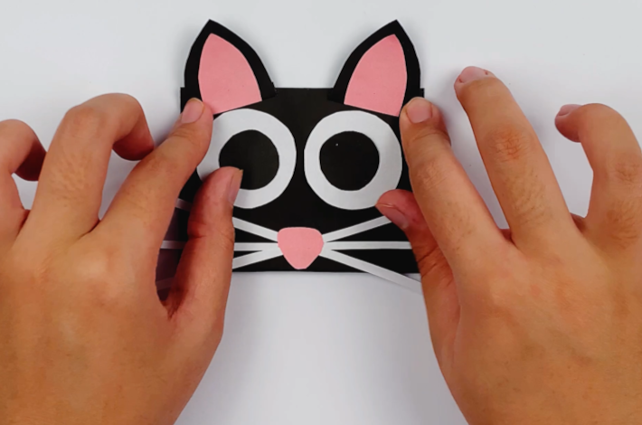 Two hands glueing the ears to the top of the cat's face.