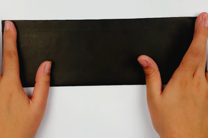 Two hands folding the top section of the paper with the glue downwards to secure it to the bottom section.