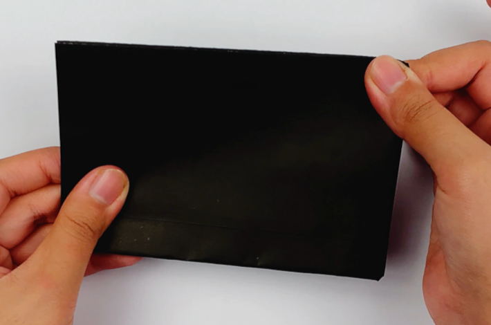 Two hands folding the black paper over from right to left to form a smaller rectangle.