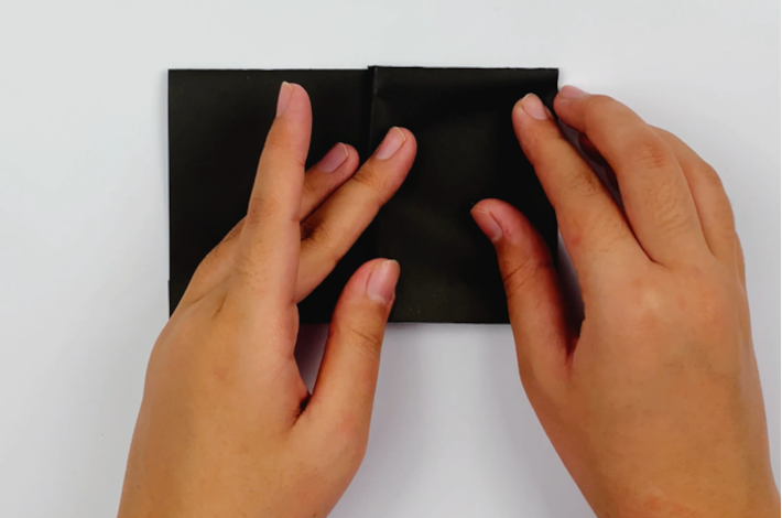 Two hands folding the top section of the paper on the left in half back towards the right-hand side