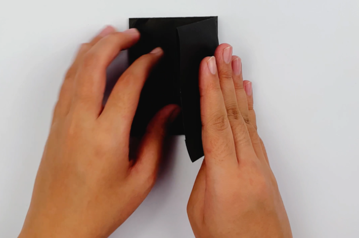 Two hands flipping the paper 180 degrees and folding the other side over to form a smaller rectangle.