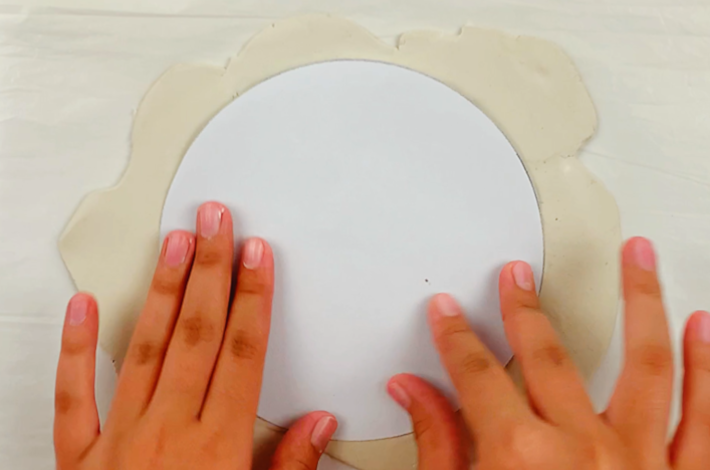 Two hands placing a plate in the center of the modeling clay.