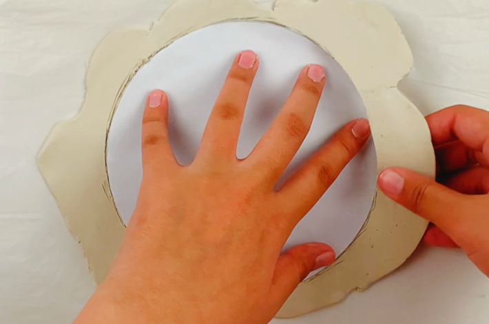 Two hands removing the excess clay. 