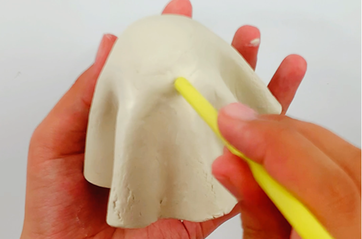 Two hands making a hole in the modeling clay for the nose.