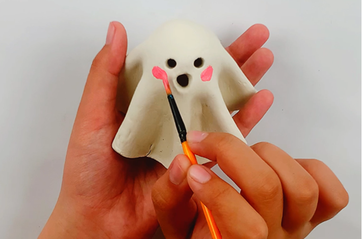 Two hand painting pink cheeks on the ghoast. 