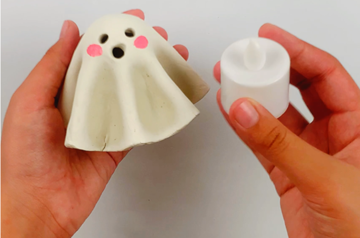 Two hands holding the ghost as well as a battery-powered candle light.