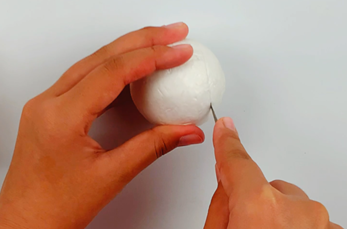 Two hands cutting the narrow end off the styrofoam egg using a hobby knife. 