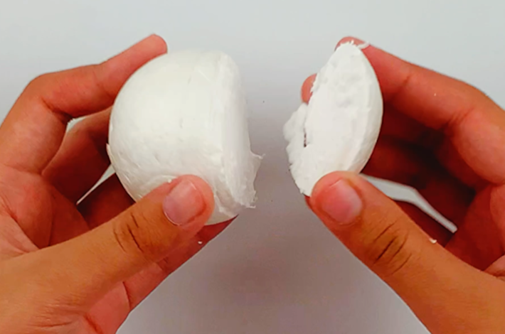 Two hands separating the narrow side of the craft styrofoam egg