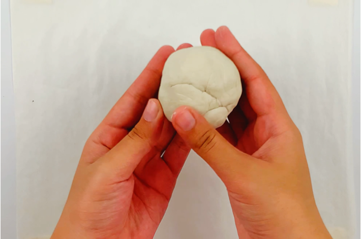 Two hands forming the modeling clay into a ball.
