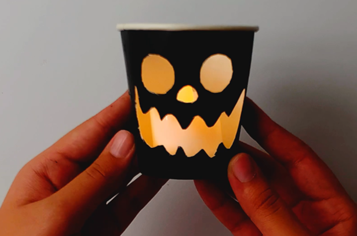 Two hands holding the paper cup with the battery powered candle light inside. 
