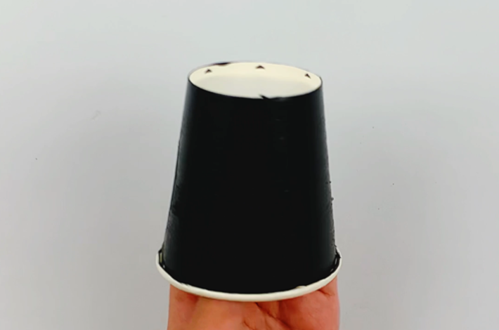 Two hands holding up the finished painted paper cup. 